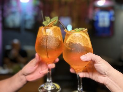 Two orange cocktails raised in a toast at the bar
